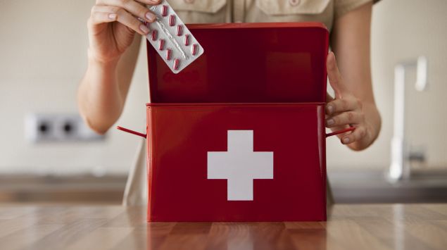 Das Bild zeigt eine Frau, die eine Packung Tabletten in einen Erste-Hilfe-Koffer packt.