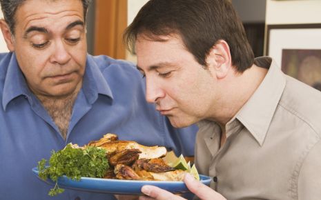 Ein Mann riecht an einem Teller mit Essen, ein anderer steht daneben.