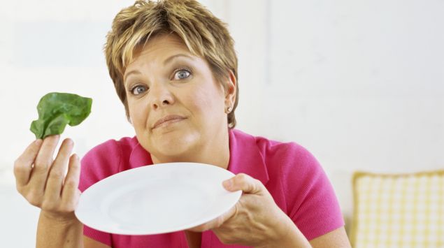 Das Bild zeigt eine Frau mit leerem Teller und einem Salatblatt in der Hand.