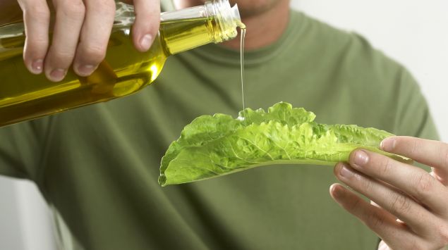 Das Bild zeigt einen Mann, der Öl auf ein Salatblatt gießt.