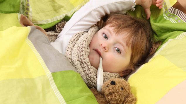 Das Bild zeigt einen Jungen, der mit Fieberthermometer im Bett liegt.