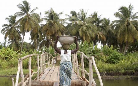 Onchozerkose: Eine afrikanische Frau trägt eine Schüssel über eine Brücke.