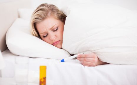 Pfeiffersches Drüsenfieber: Eine Frau liegt im Bett und liest das Fieberthermometer ab.