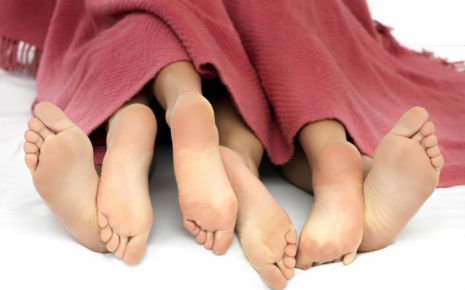 Sechs nackte Füße schauen unter einer Decke hervor.