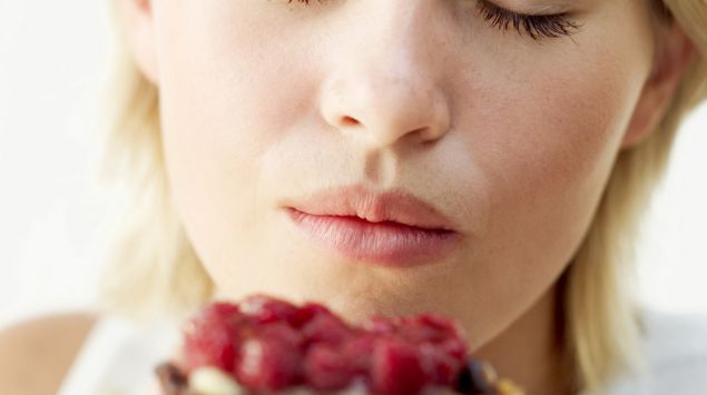 Man sieht eine Frau, die mit geschlossenen Augen in ein Obsttörtchen beißt.