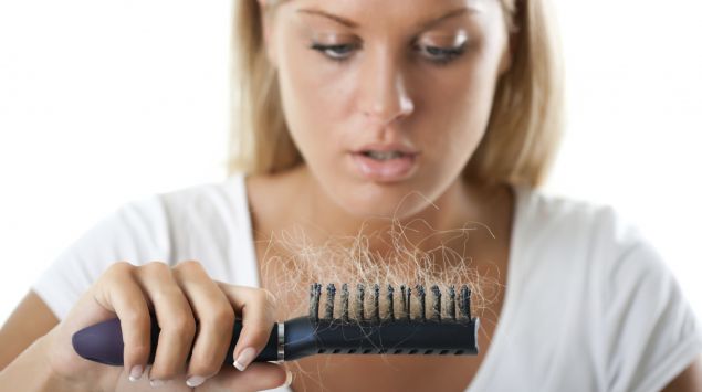 Man sieht eine Frau, die auf ausgefallene Haare in ihrer Haarbürste starrt.
