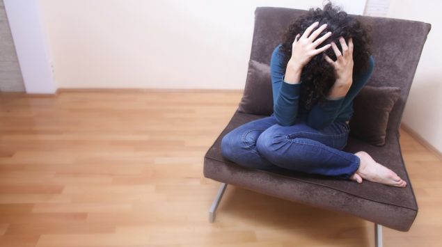 Man sieht eine Frau, die auf einem Sessel sitzt und die Hände über dem Kopf zusammenschlägt.