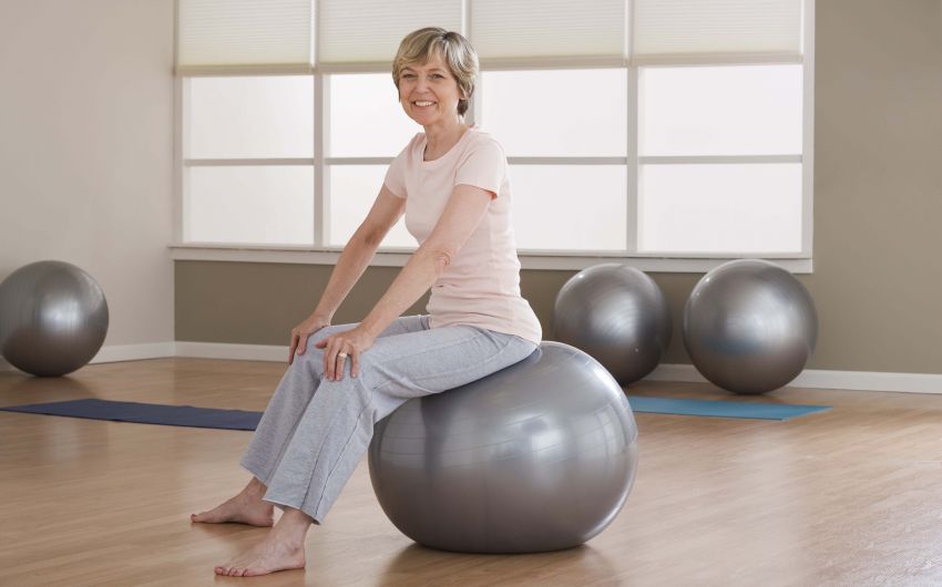 Rückenschmerzen: EIne ältere Frau sitzt aufrecht auf einem Gymnastikball.