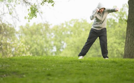 Ein Mann steht in Sportkleidung auf einer Wiese und boxt in die Luft.