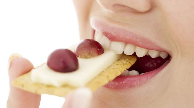 Eine Frau isst einen Cracker mit Käse und Weintrauben.