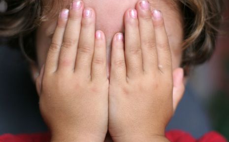 Ein Kind verdeckt seine Augen mit den Händen.