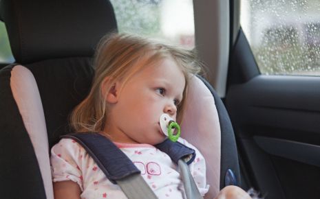 Man sieht ein Kind im Auto in einem Kindersitz.