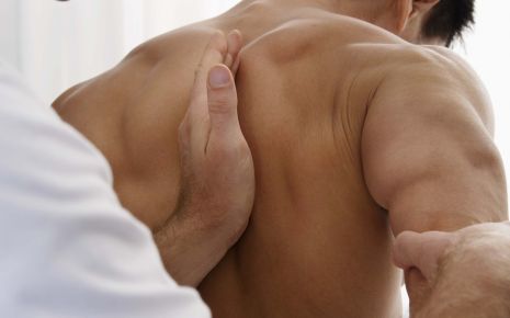 Ein Krankengymnast arbeitet im Schulterbereich eines Patienten.