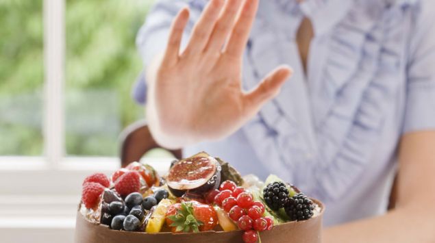 Eine Frau lehnt mit einer Handbewegung das ihr angebotene Essen ab.