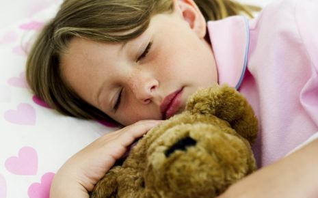 Ein Mädchen schläft im Bett und hält einen Teddy im Arm.