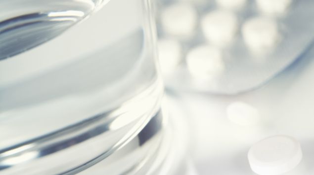 Das Bild zeigt mehrere Tabletten neben einem Glas mit Wasser.