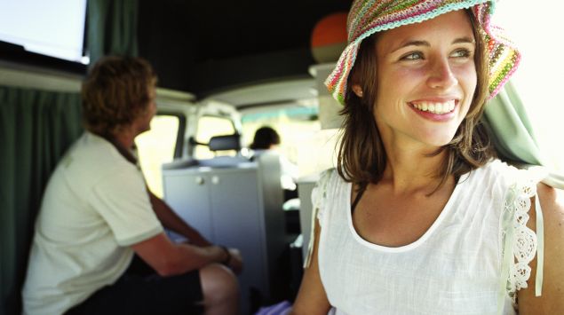 Man sieht eine lachende Frau mit Sonnenhut in einem Campingbus.
