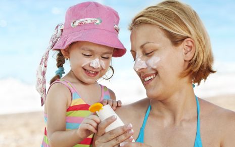 UV-Strahlung: Ein Mädchen mit seiner Mutter am Strand, es trägt einen Sonnenhut, beide haben Creme im Gesicht.
