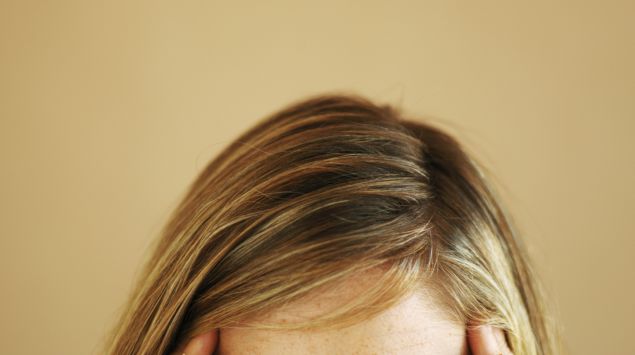 Das Bild zeigt eine blonde Frau, die ihre Hände an die Schläfen hält.