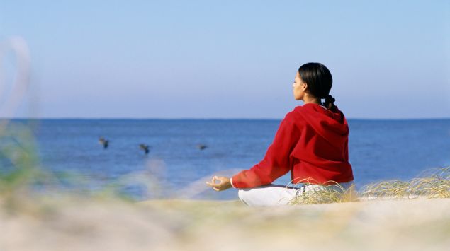 Das Bild zeigt eine Frau im Schneidersitz am Meer.