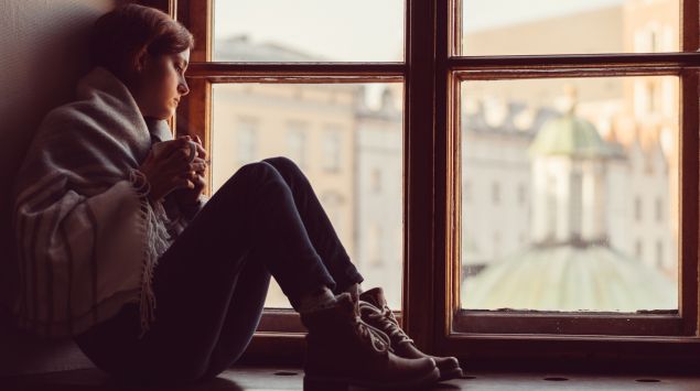 Junge Frau sitzt deprimiert in Fensternische.