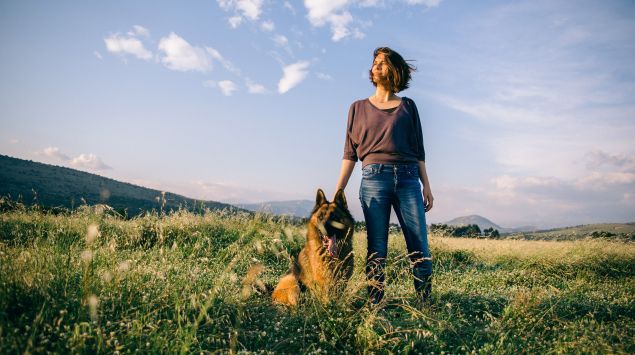 Das Bild zeigt eine Frau mit ihrem Schäferhund auf einer Wiese