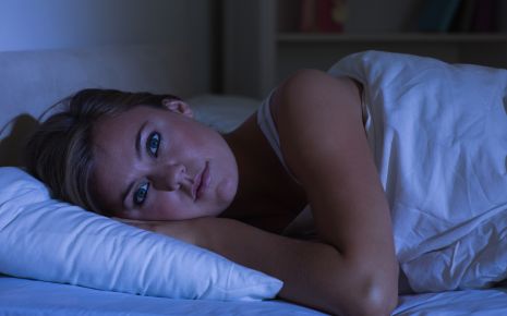Man sieht eine junge Frau, die mit offenen Augen im Bett liegt.