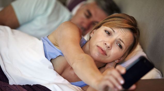 Eine schlaflose Frau blickt auf ihr Smartphone.