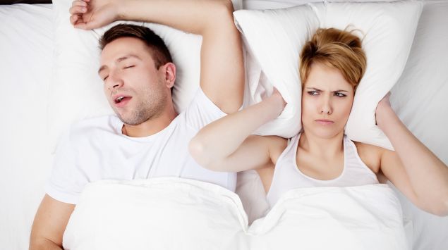 Mann schnarcht, Frau leider darunter im Bett und hält sich die Ohren zu