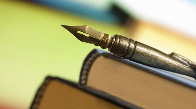 Auf einem Stapel Bücher liegt eine alte Schreibfeder.