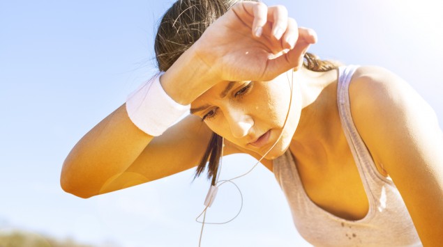 Eine junge Frau im Trainingsoutfit wischt sich den Schweiß von der Stirn.