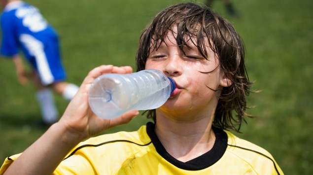 Verschwitzter Junge trinkt beim Fußballspiel Wasser.