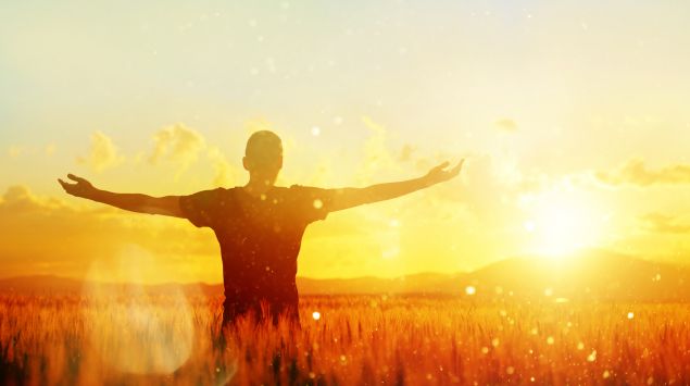 Mann breitet im sonnenüberfluteten Feld die Arme aus