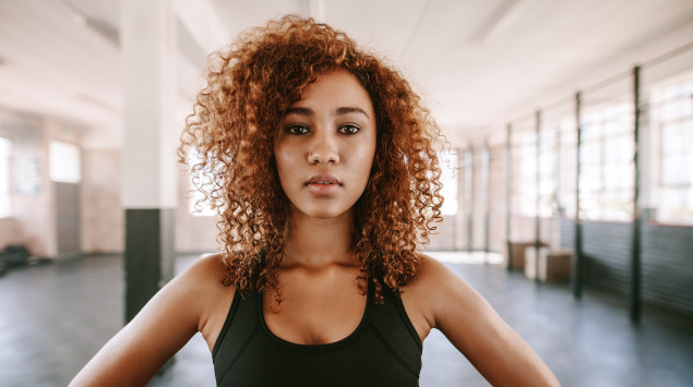 Eine Frau mit dunklen Locken und sportlichem Outfit blickt gerade in die Kamera.