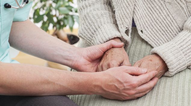 Man sieht eine Ärztin, die einer älteren Frau die Hand hält.