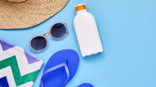 Zusammenstellung von Sonnenhut, Sonnenbrille, Sonnencreme, Sandalen