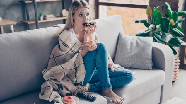 Eine junge Frau sitzt auf dem Sofa und isst Donuts.