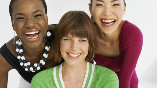 Eine afrikanische, eine europäische und eine asiatische Frau lachen in die Kamera