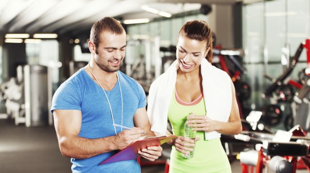 Das Bild zeigt einen Fitnesstrainer mit einem Trainingsplan in der Hand.