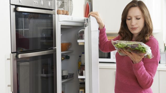 Bakterienschleuder oder gesunder Snack? Eine Frau blickt kritisch auf eine Packung Salat, die sie gerade auch dem Kühlschrank geholt hat.