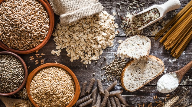 Tisch mit verschiedenen Vollkornprodukten wie Haferflocken, Nudeln und Brot