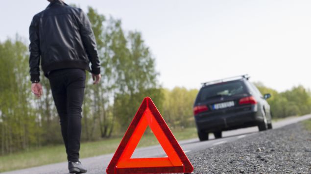Ein Mann läuft von einem Warndreieck zurück in Richtung Auto.