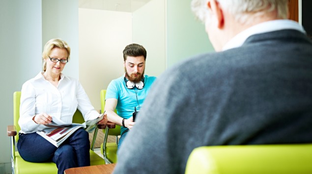 Eine Frau, ein jüngerer und ein älterer Mann sitzen in einem Wartezimmer.
