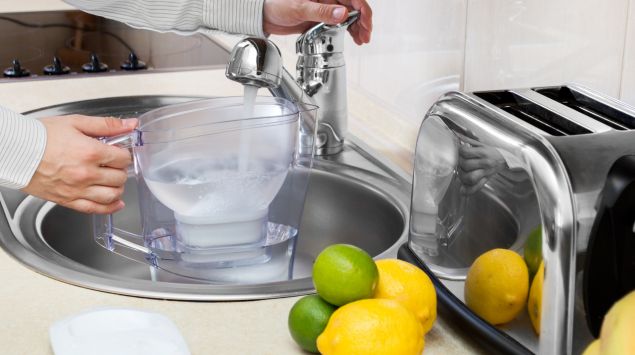 Ein Mann füllt einen Wasserfilter-Behälter mit Leitungswasser.