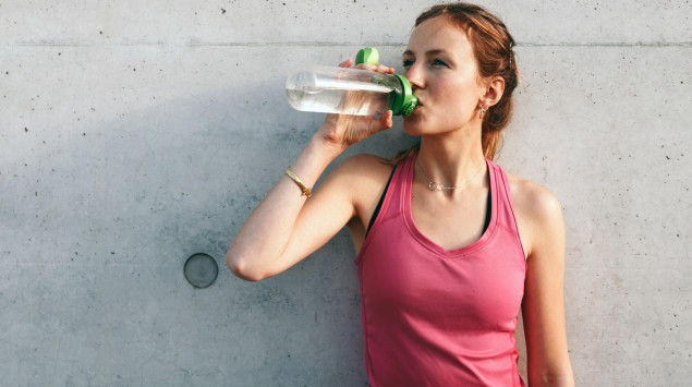 Eine Frau trinkt aus einer Wasserflasche: Kann man Wasser auf Vorrat trinken?