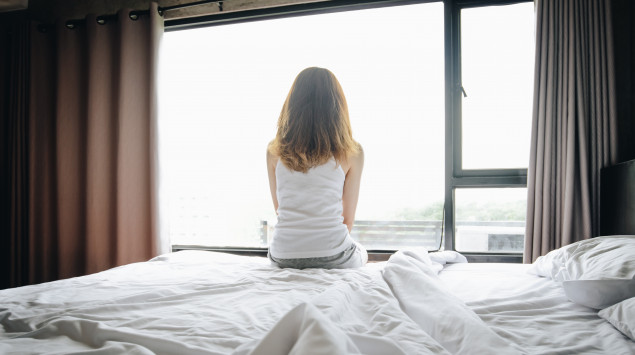 Frau sitzt aus dem Bett und schaut aus dem Fenster