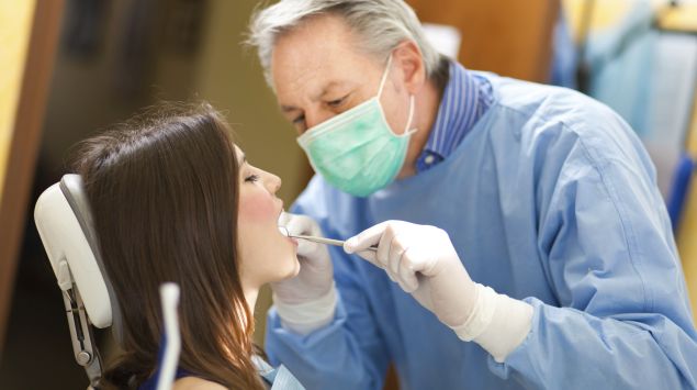 Ein Zahnarzt schaut in den Mund seiner Patientin.