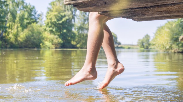 Jemand sitzt auf einem hölzernen Steg an einem See und hält seine Zehen ins Wasser.